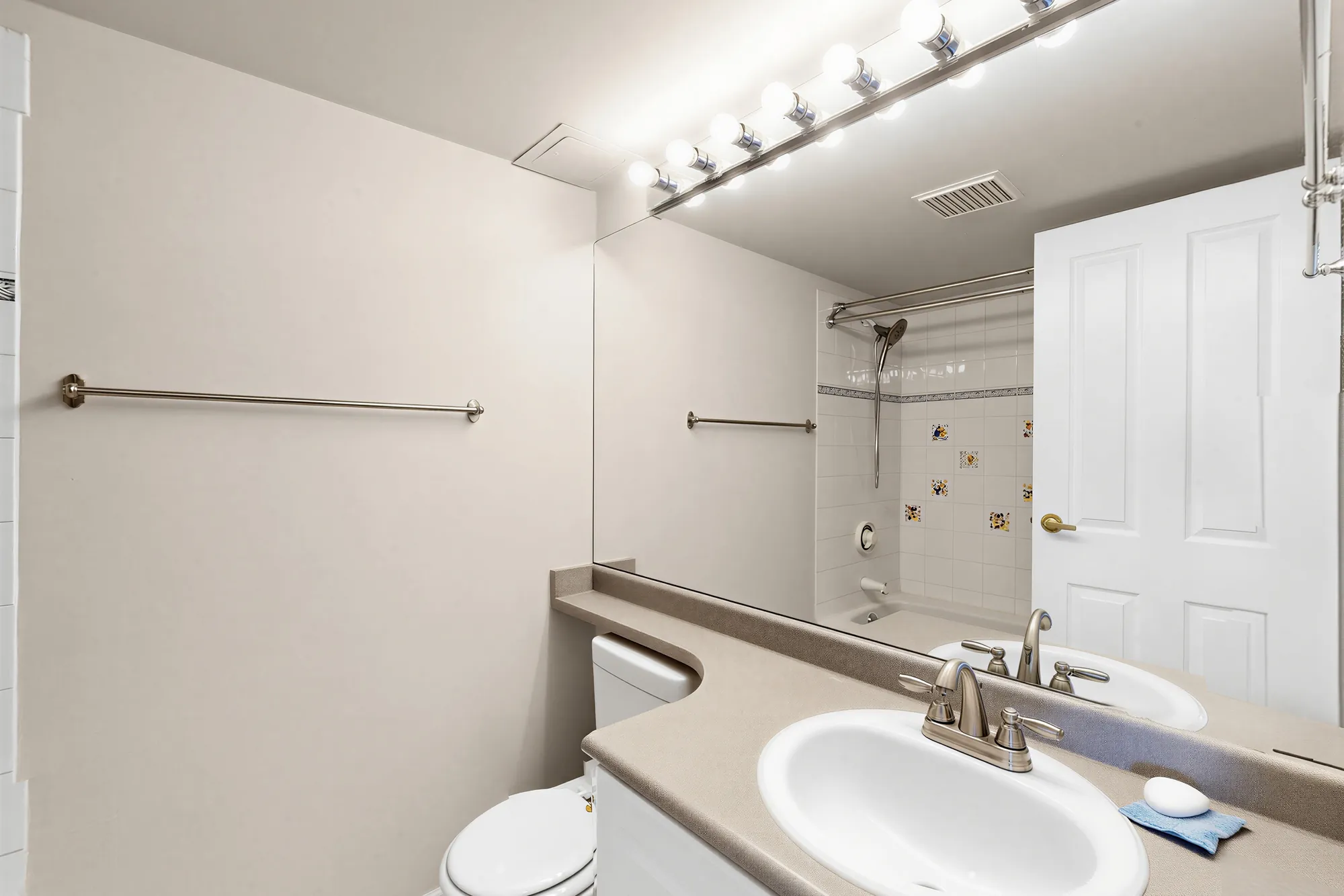 A bathroom with a tub and shower, mirror running the width of the wall