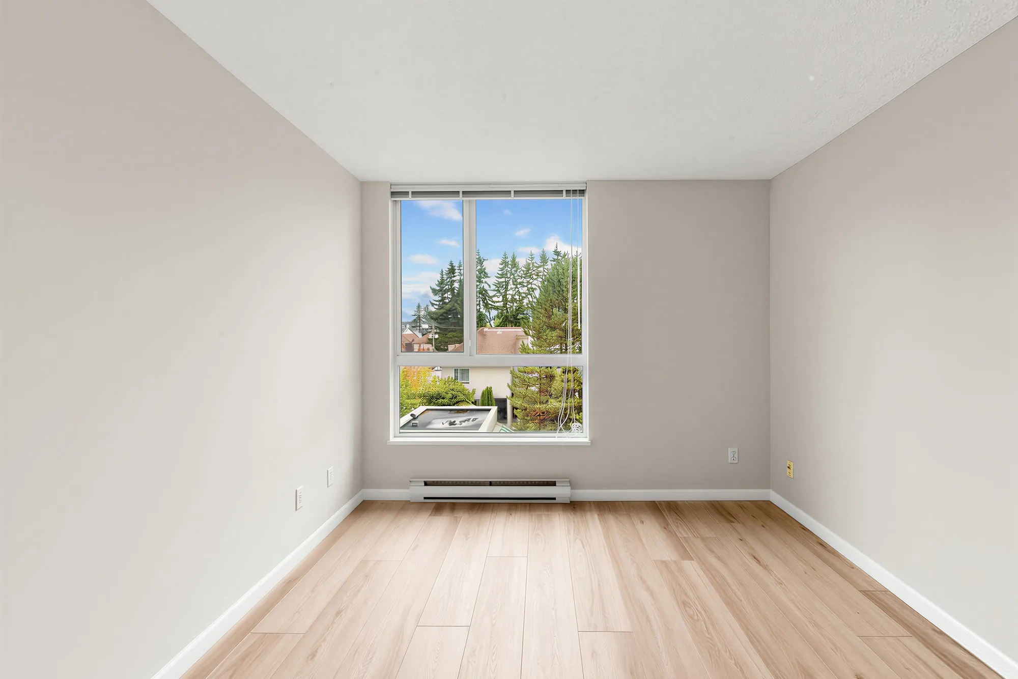 A bedroom with a window onto the trees and a baseboard heater below it