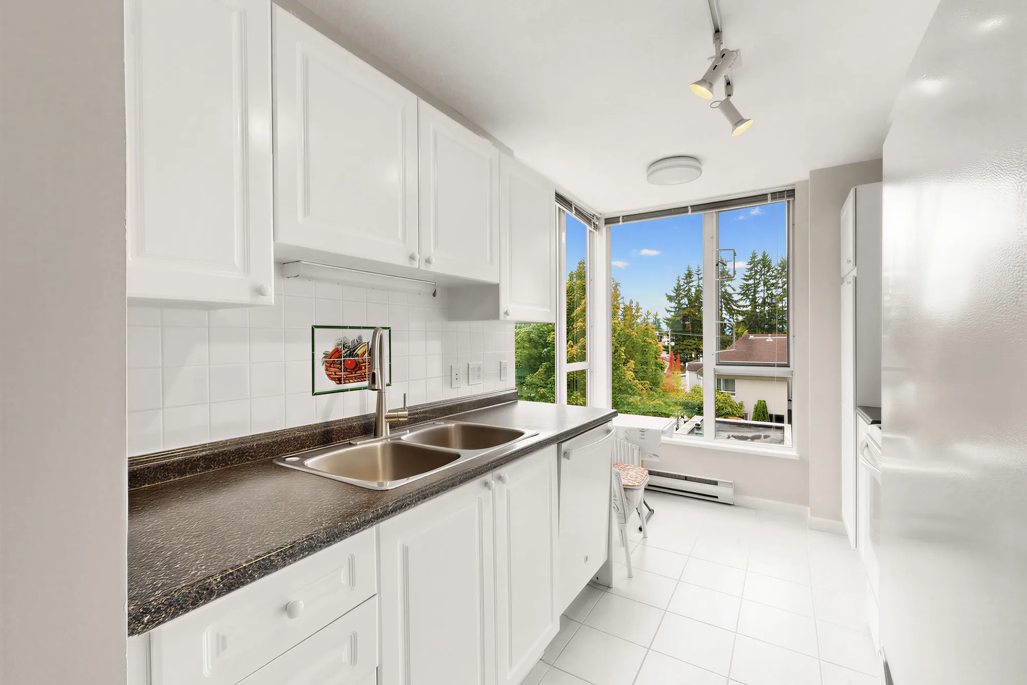 The kitchen with white cabinets, dark counters and a window over the sink